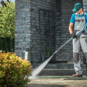 Driveway Pressure Washing. Caucasian Worker Cleaning Area in Front of the House.